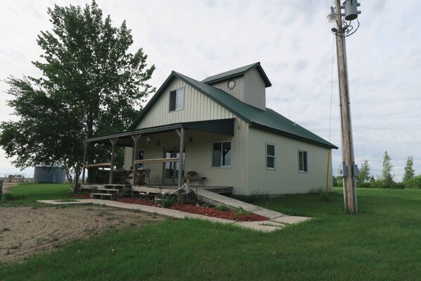 A two-story house with a porch, a small front yard, and a utility pole. - Rural Getaway at Homestead Lodge (Bottineau)