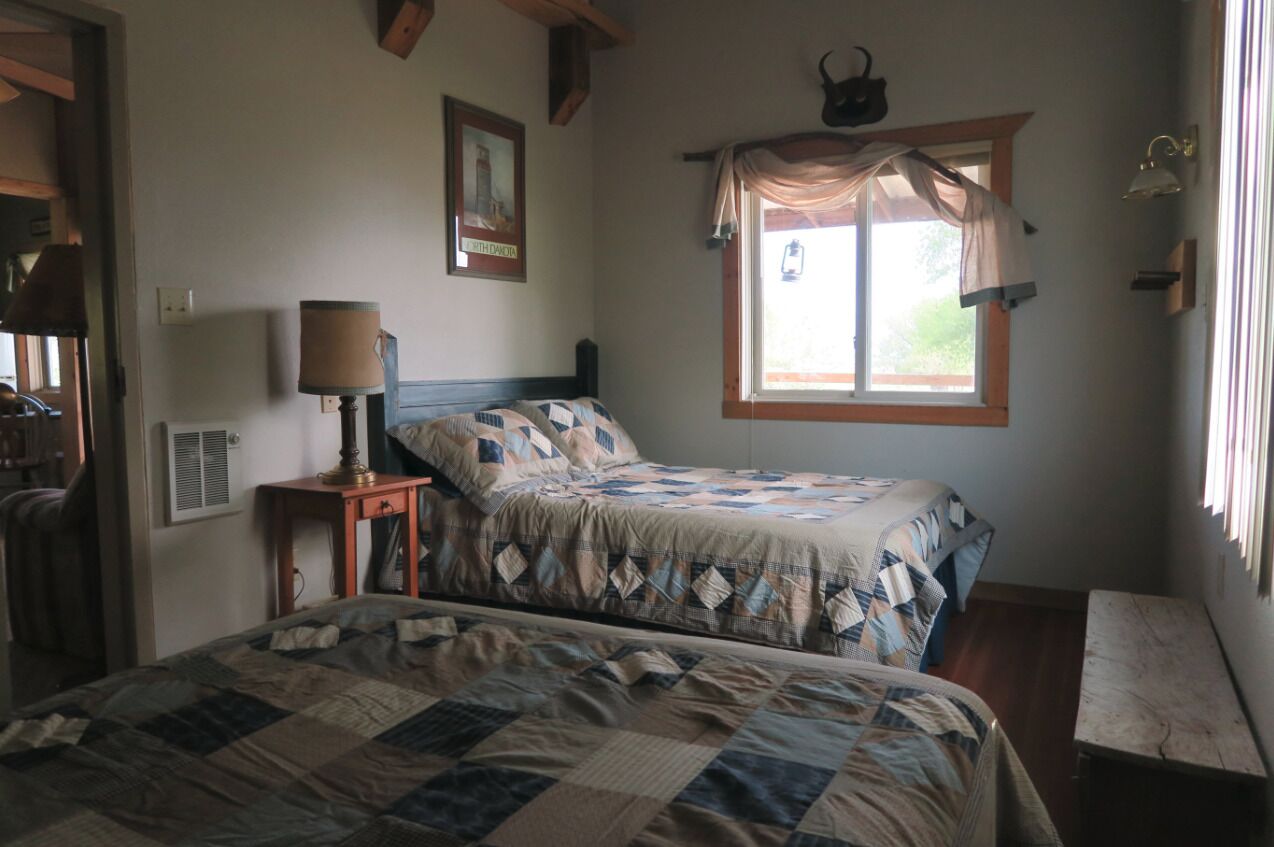 Ein Schlafzimmer mit zwei Betten, einem Fenster mit Vorhang, einem Nachttisch mit Lampe und einer Wandleuchte.