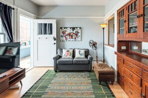 Ein Wohnzimmer mit grauem Sofa, einem gemusterten Teppich, einer Holzkabine und einem Gemälde an der Wand.