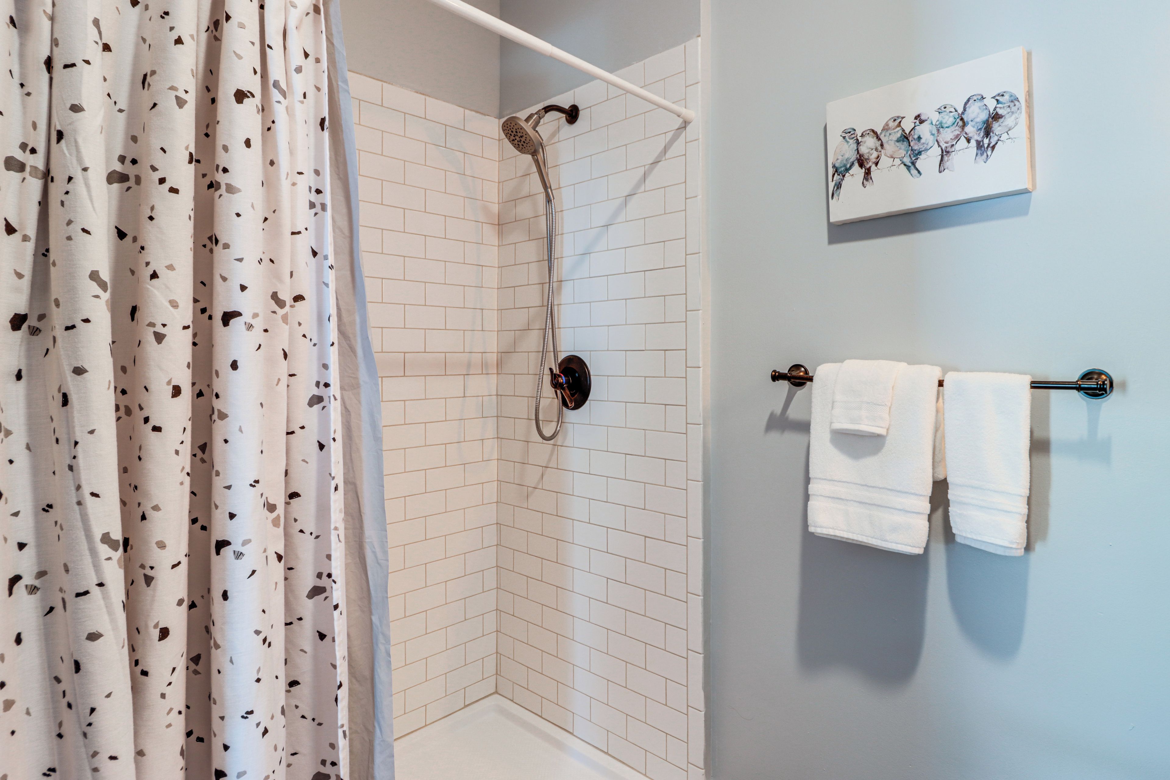 Une douche avec un mur recouvert de carreaux blancs et un pommeau de douche.