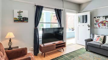 A living room with a flat-screen TV, a leather armchair, a sofa, a patterned rug, and artwork on the walls.