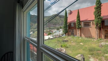 A window view of a house with a red roof, a brick exterior, and a grassy yard with a stone wall.