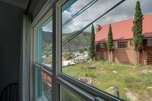 Vista da janela de uma casa com telhado vermelho, fachada de tijolos e um gramado com muro de pedra.