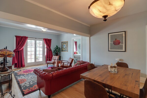A living room with a red sofa, a wooden dining table, and a chandelier. - 'St Valentine' Apartment w/ Balcony in Bisbee (Bisbee)