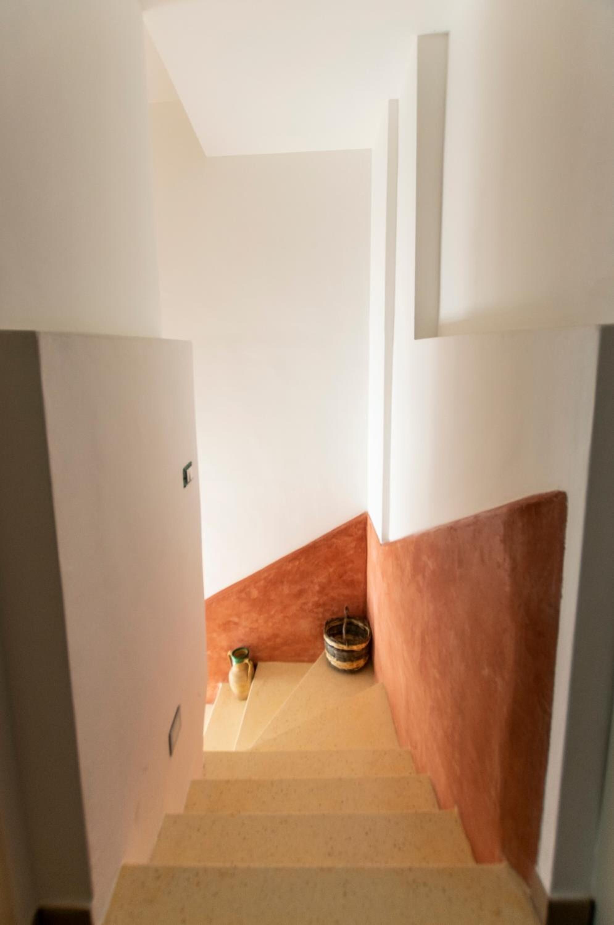 Una escalera con alfombra color beige que conduce a un rellano con dos macetas decorativas.