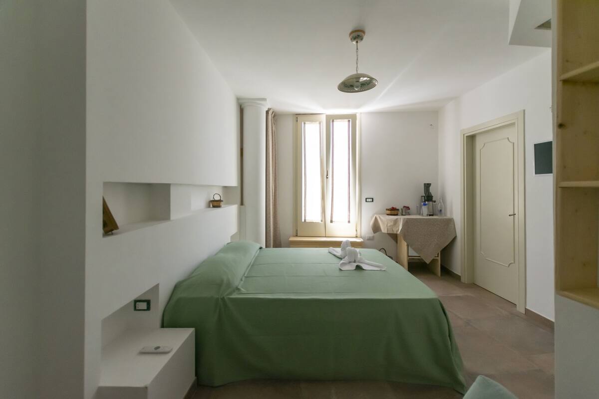 Ein kleiner, heller Raum mit einem Bett, einem Tisch mit Tischdecke und einer Tür.