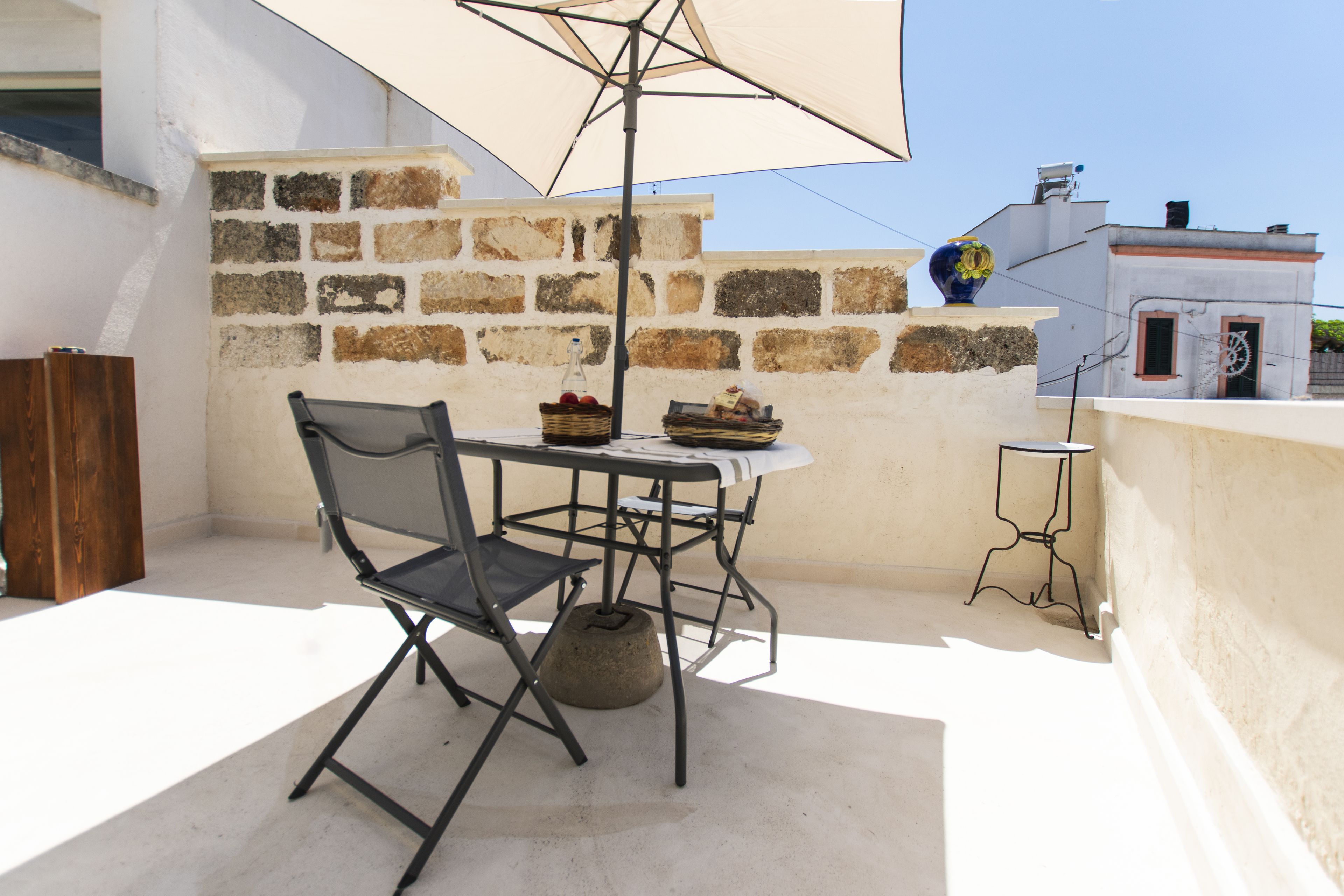 Un pequeño patio al aire libre con una mesa y sillas, una cesta de mimbre con fruta y un jarrón decorativo.