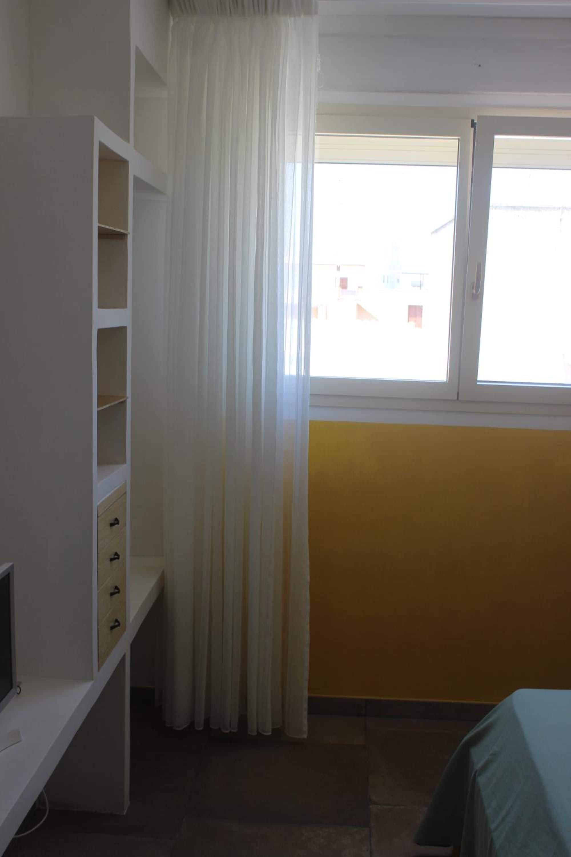 Una habitación con un armario blanco, una ventana con persiana blanca y una pared amarilla.