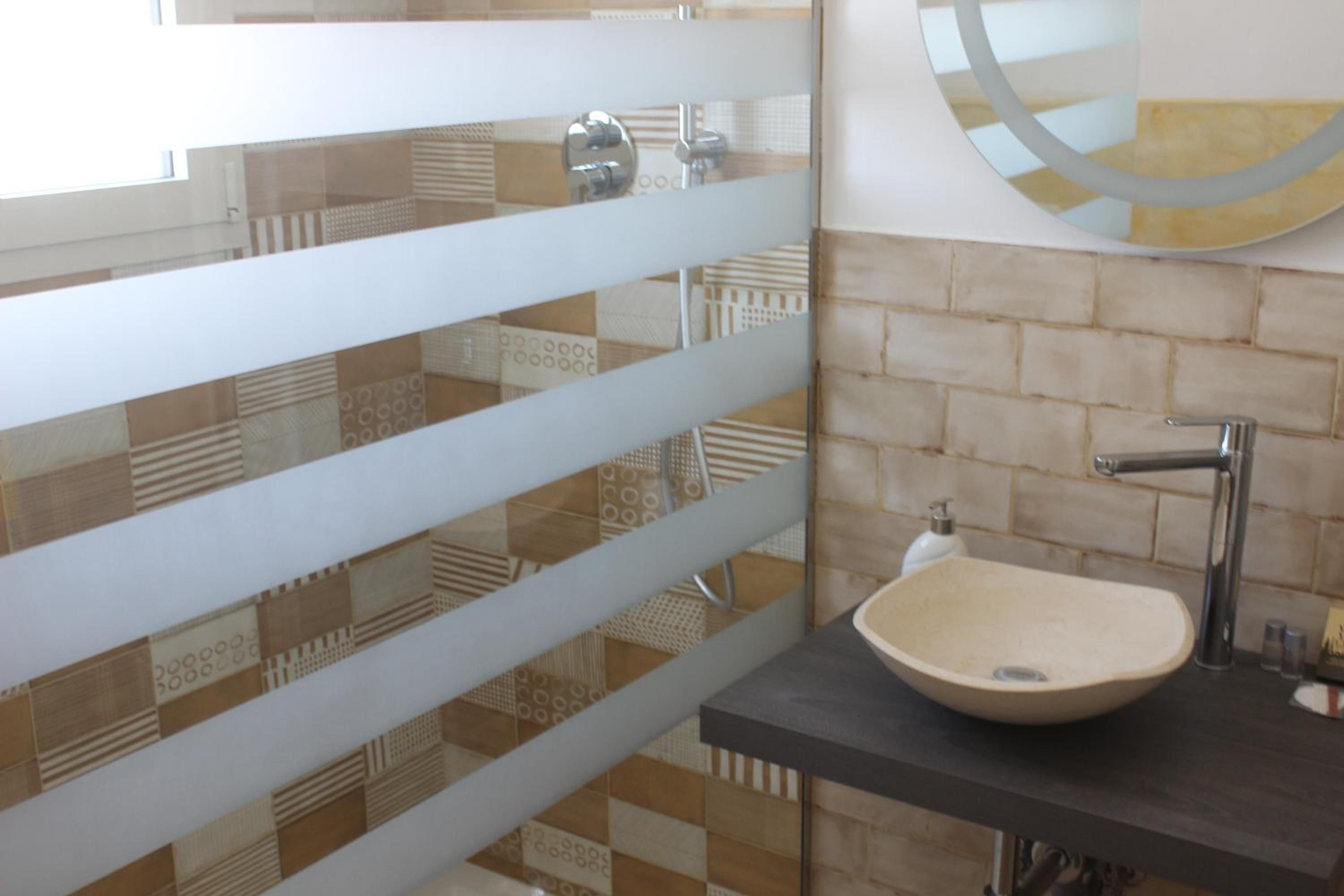 Casa de banho com azulejos estampados, lavatório suspenso, espelho e porta-toalhas.