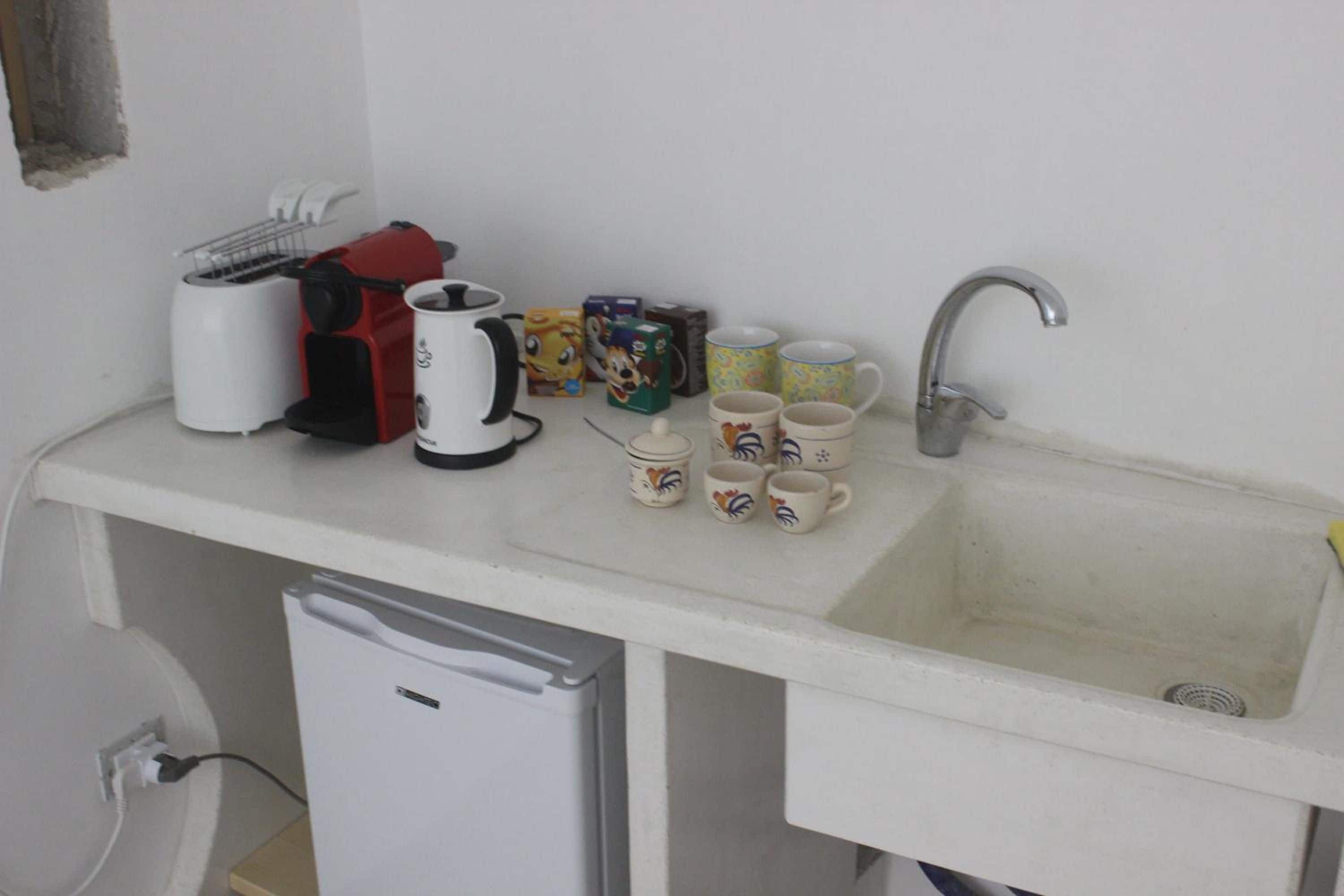 Una pequeña cocina americana equipada con cafetera, tostadora, pileta y varios vasos.
