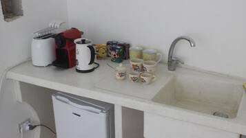 Una pequeña cocina americana equipada con cafetera, tostadora, pileta y varios vasos.