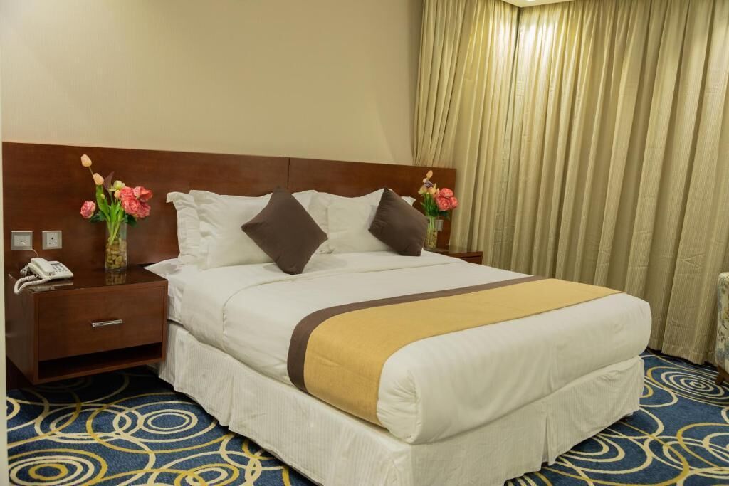 A hotel room with a bed, a nightstand with a phone, and a vase with flowers.