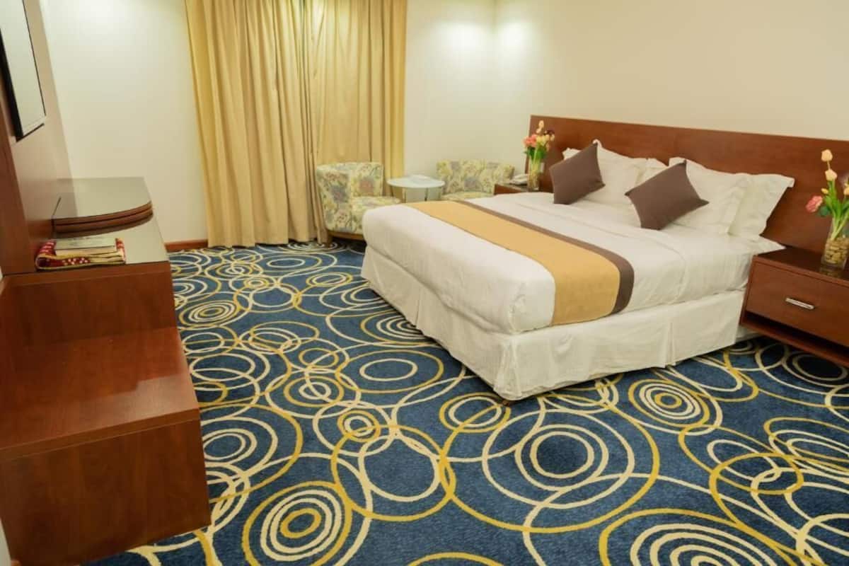 Ein Hotelzimmer mit einem großen Bett, einem kleinen runden Tisch, einem Stuhl und einem Nachttisch mit Blumen.