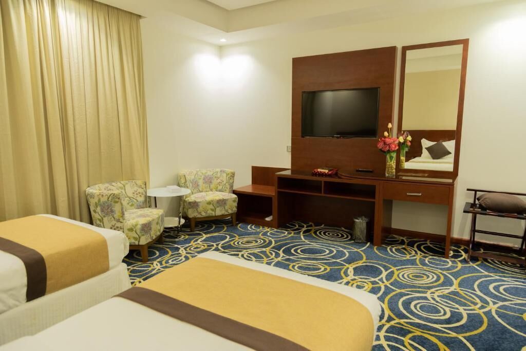 Hotellihuone, jossa on kaksi sänkyä, televisio, työpöytä, tuoli ja peili.