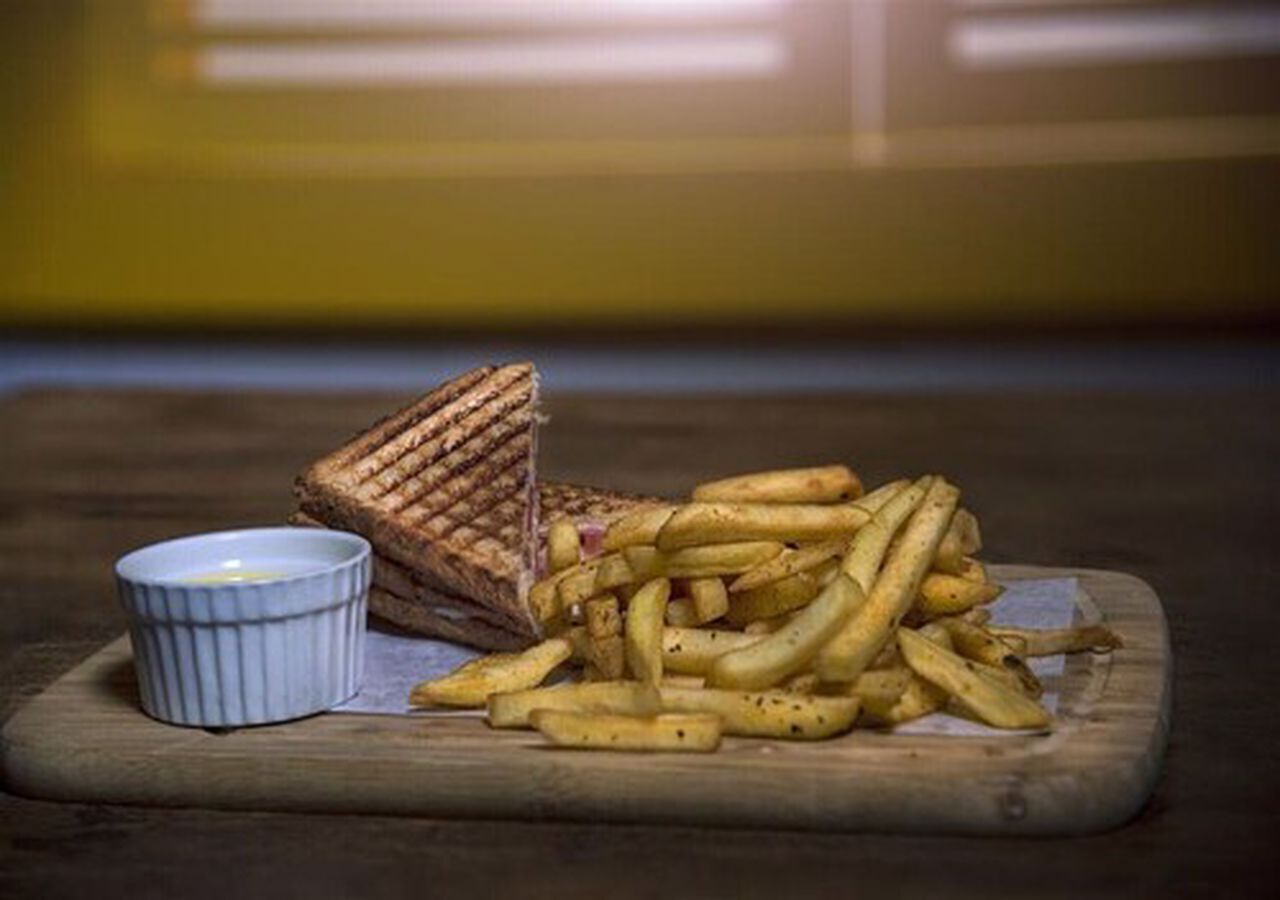 Un sándwich y papas fritas sobre una tabla de madera, con un recipiente pequeño de salsa.