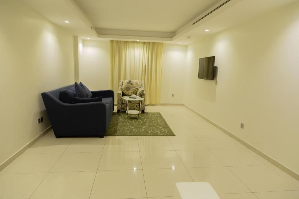 A modern living room with a sofa, a chair, a flat-screen TV, and a large window with curtains.