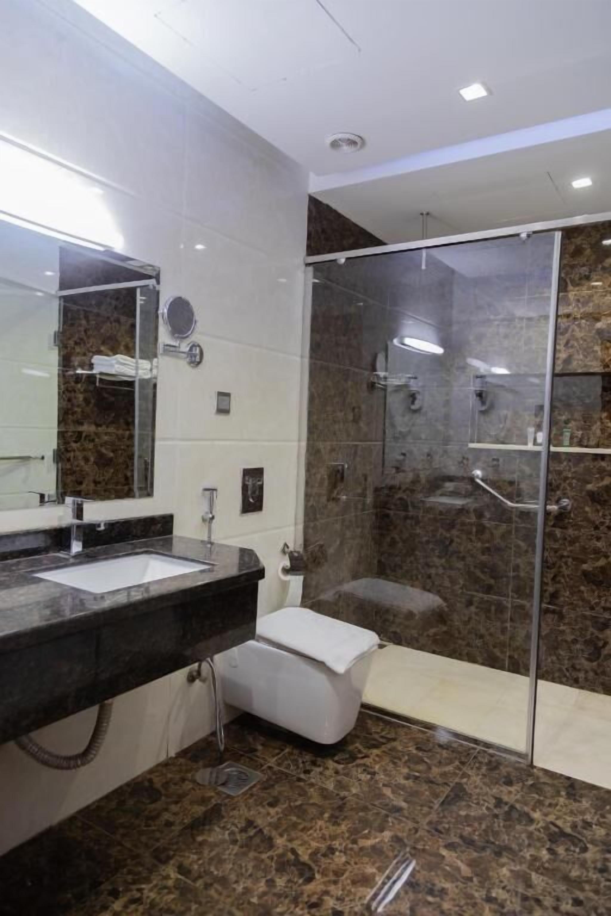 A modern bathroom with a glass-enclosed shower, a marble-tiled floor, and a white sink.