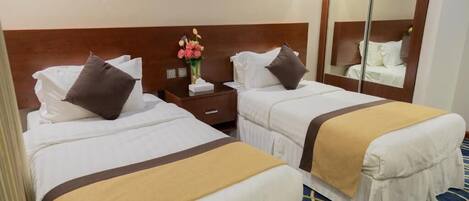 A hotel room with two beds, a nightstand, a mirror, and a vase with flowers.