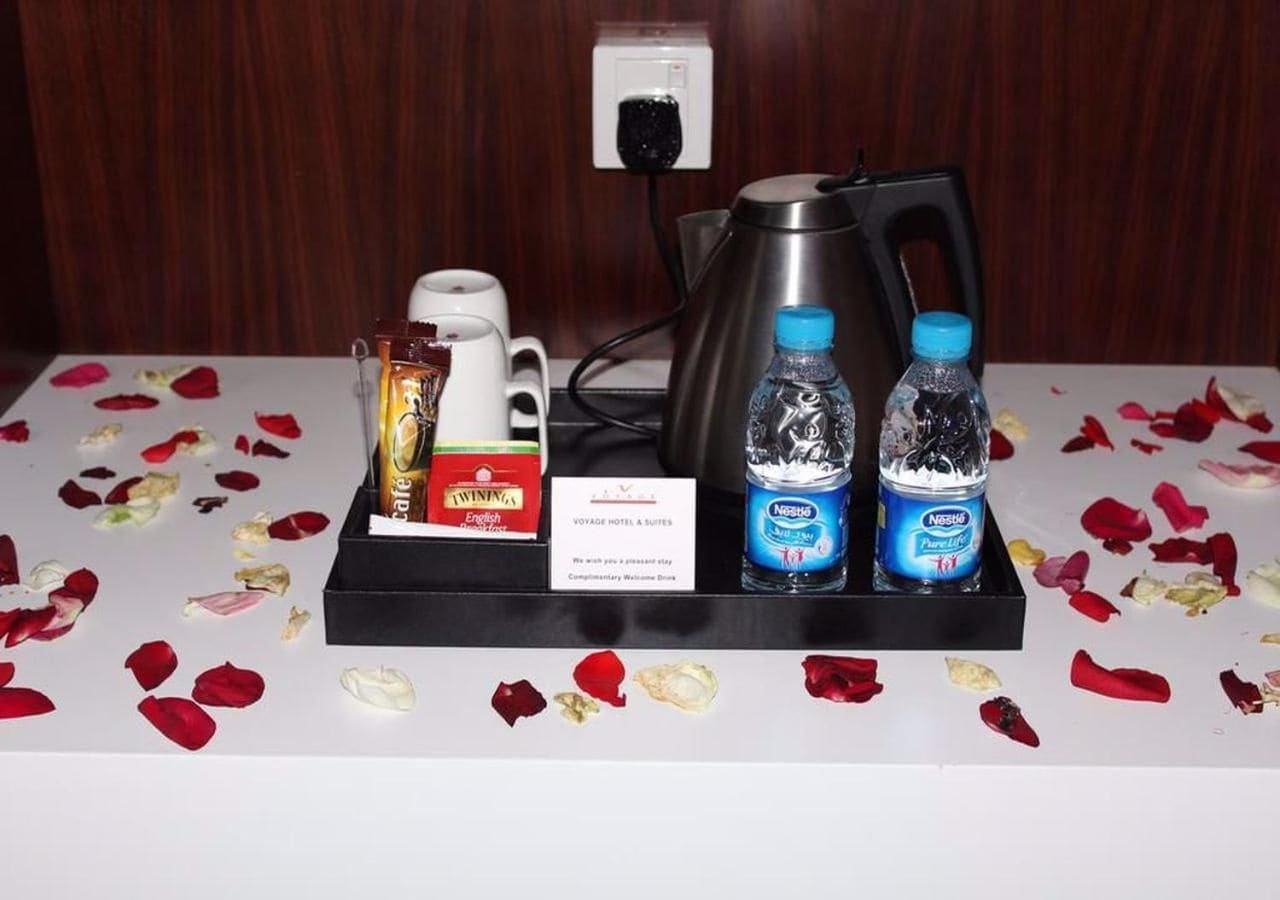 A hotel reception area with a coffee machine, two bottles of water, a box of snacks, and a sign.