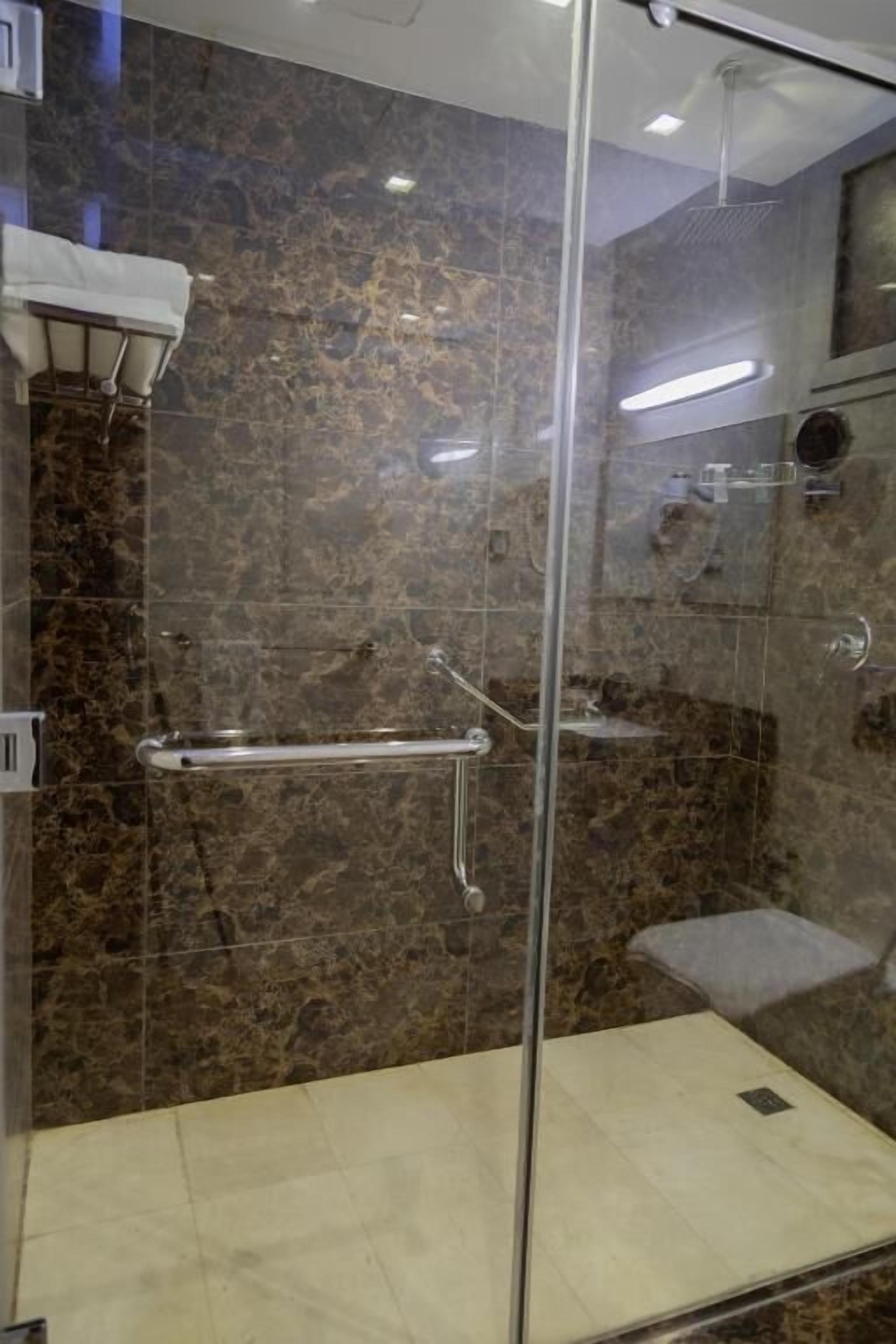 A glass-enclosed shower stall with a marble wall, a towel rack, and a glass shower head.