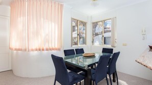 A dining area with a glass table and six chairs, two windows with blinds, and a ceiling light. - Haven Waters 6 - On the Lake! (Forster)