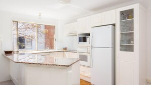 A modern kitchen with white cabinetry, a granite countertop, a built-in microwave, and a refrigerator. - Haven Waters 6 - On the Lake! (Forster)