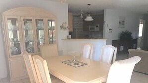 Ein Essbereich mit Holztisch und -stühlen, einem Schrank mit Glastüren und einer Küche im Hintergrund.