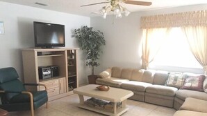 Ein Wohnzimmer mit Sofa, Couchtisch, Fernseher, Pflanze und Deckenventilator.