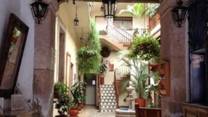 An indoor courtyard with an arched entrance, tiled flooring, potted plants, a staircase, and a fountain. - Hotel Atilanos (Morelia)