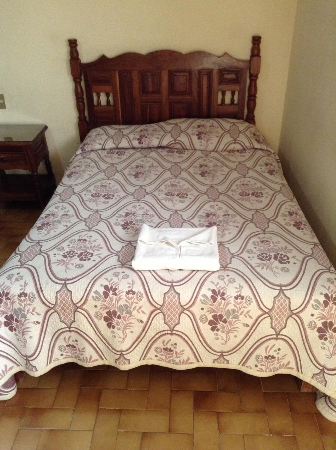 Cama bem arrumada com colcha estampada e toalha branca dobrada.