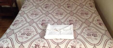 A neatly made bed with a patterned bedspread and a folded white towel.