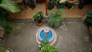 A courtyard with a fountain, potted plants, and a patterned floor. - Hotel Atilanos (Morelia)