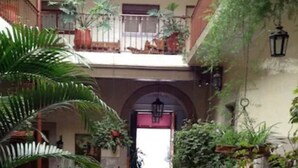 A courtyard with a fountain, potted plants, and a view of a car through an open doorway. - Hotel Atilanos (Morelia)