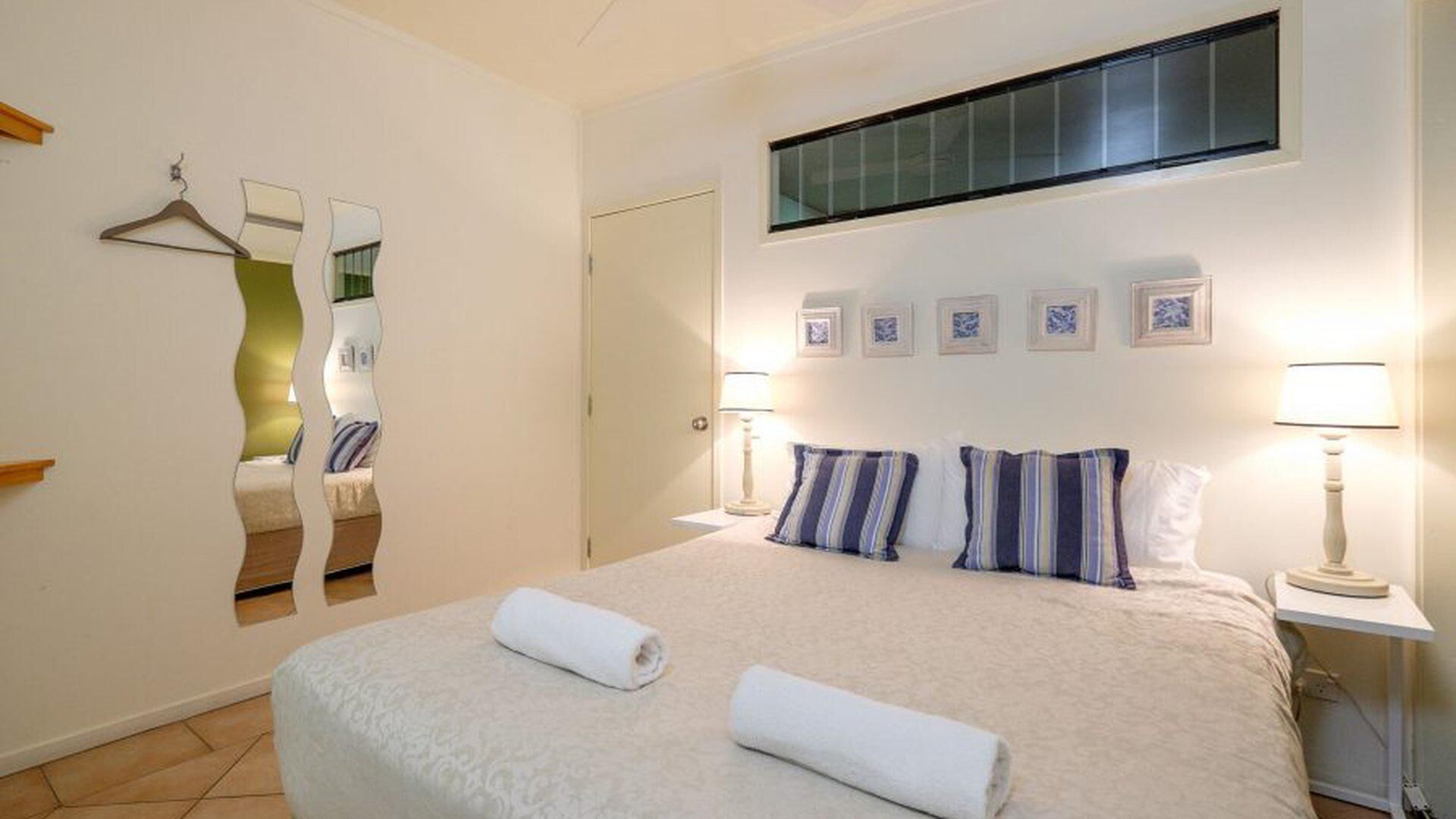 A hotel room with a large bed, two bedside lamps, a mirror, and a window.