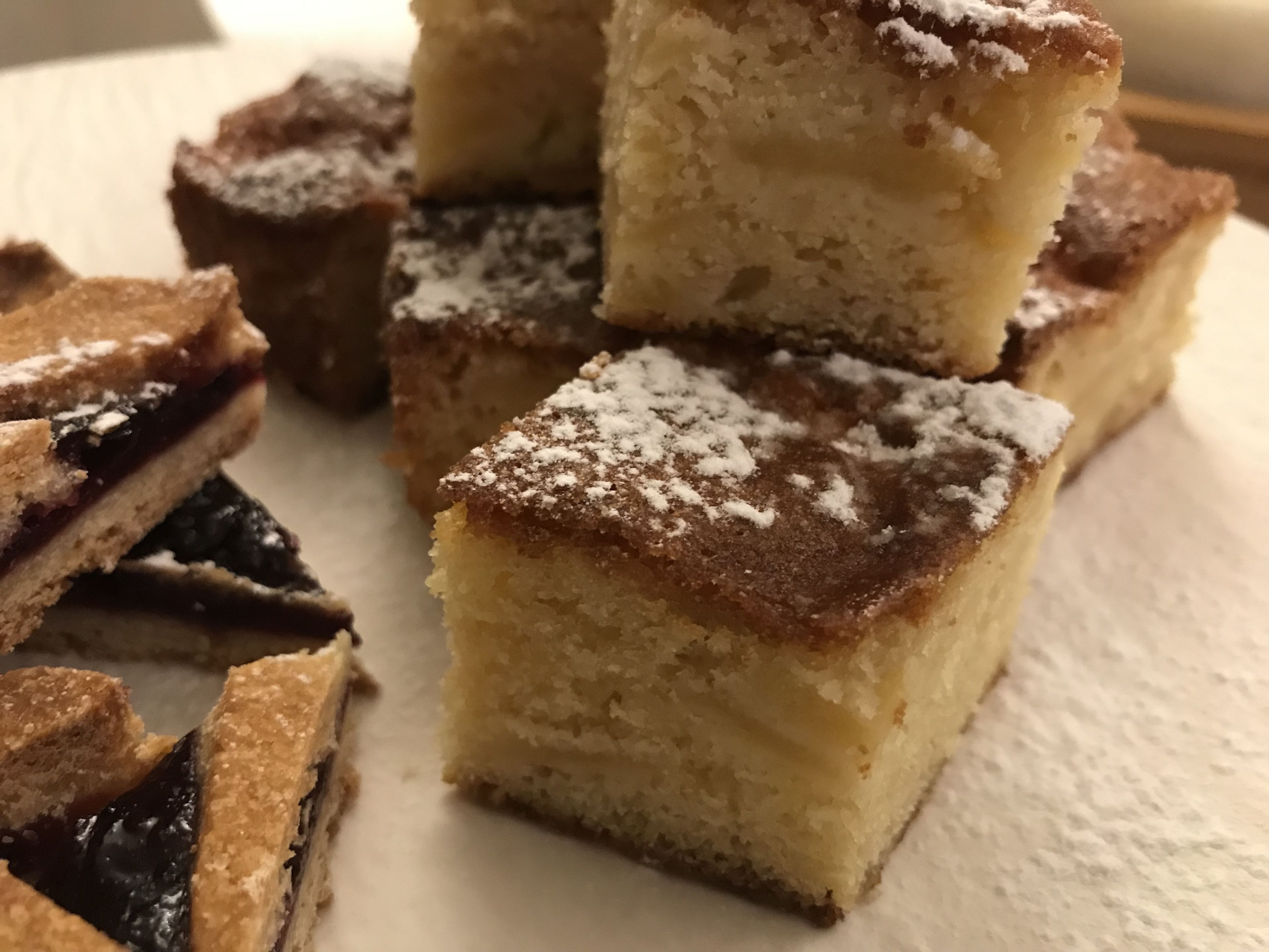 A close-up of several square desserts, possibly cake, with powdered sugar on top, arranged on a white surface.