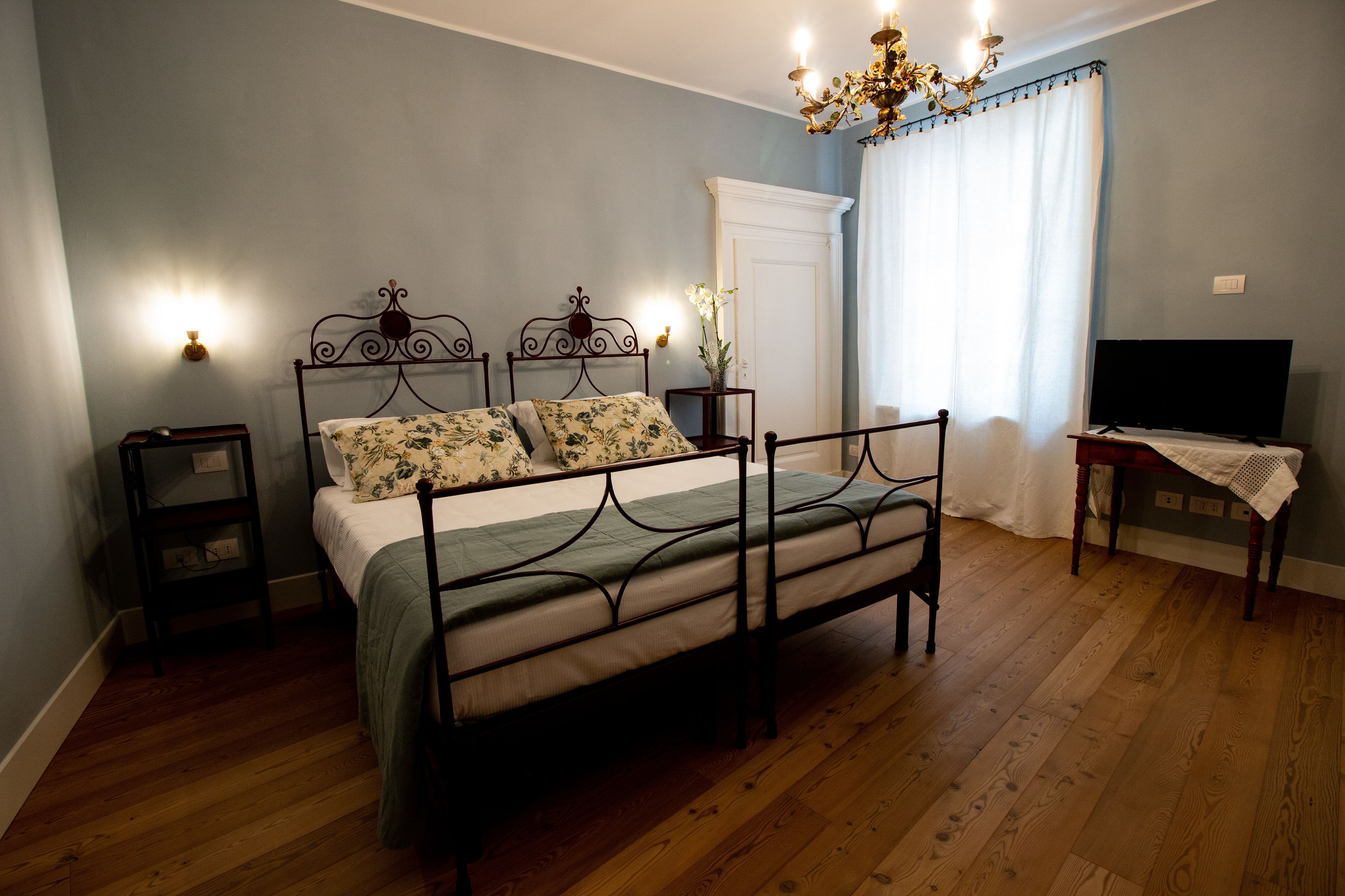 A bedroom with a four-poster bed, a television on a wooden stand, and a chandelier.