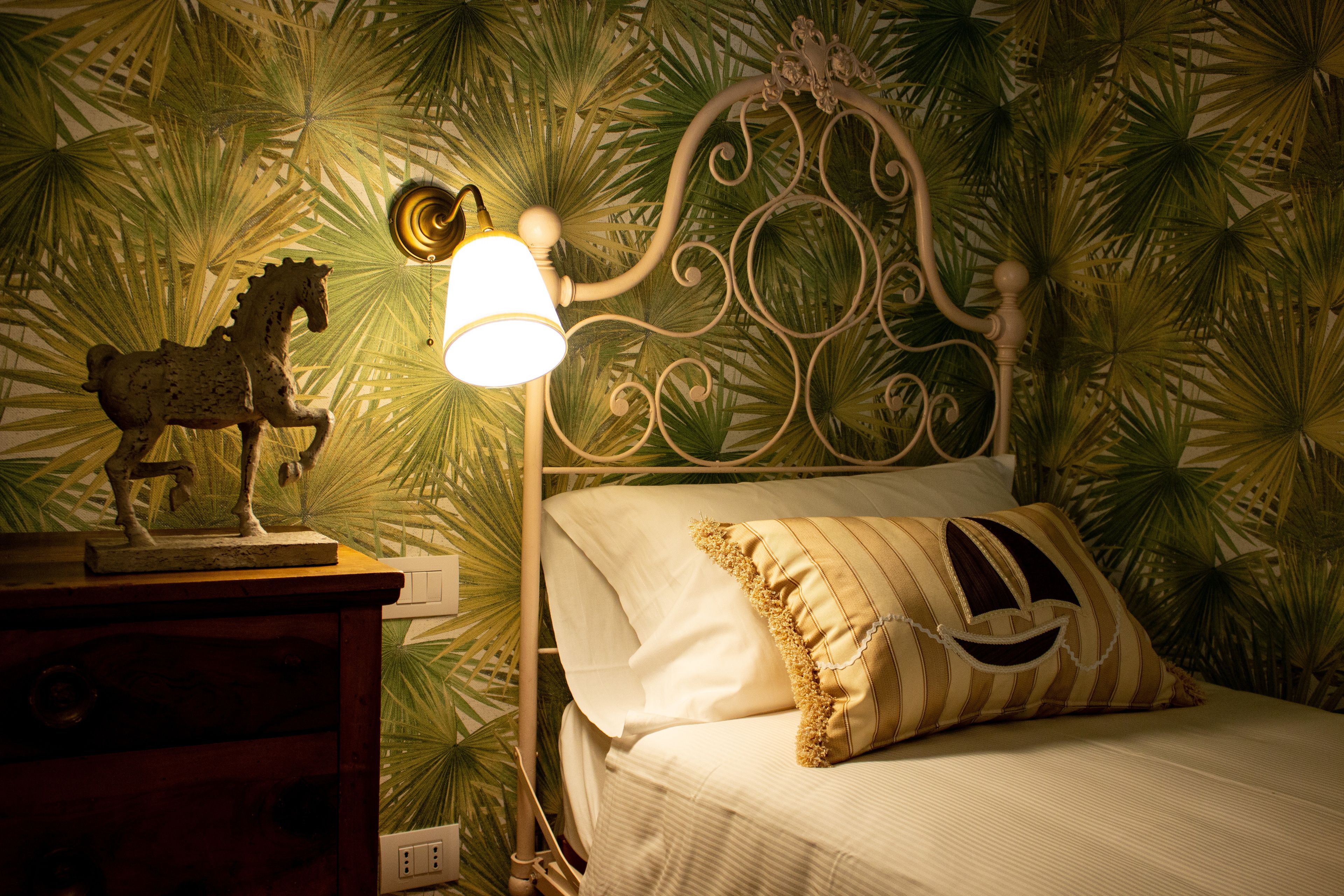 Een bed met een decoratief hoofdbord, een nachtkastje met een beeldje van een paard, en een wand met een bladmotief.