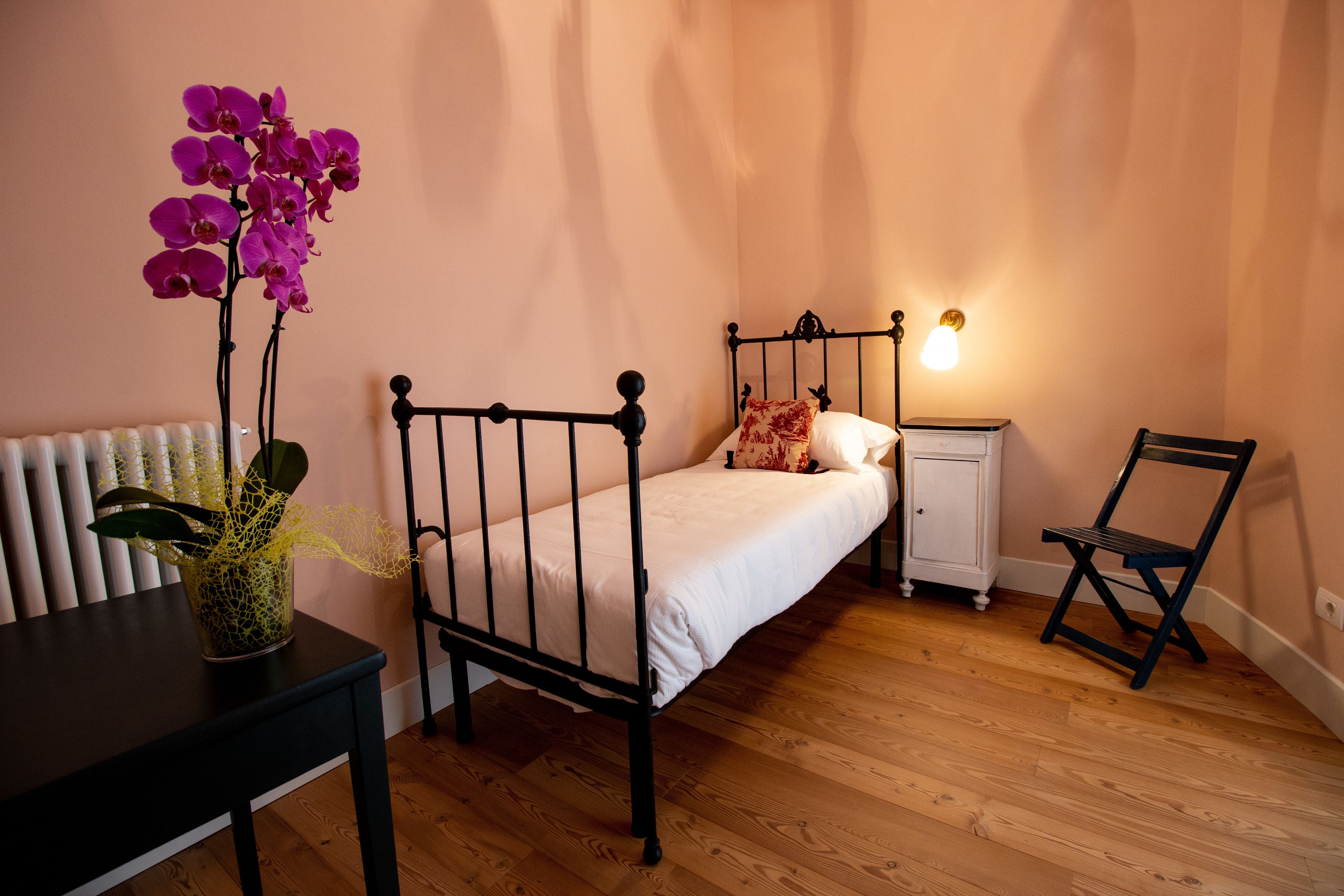 Un dormitorio con cama, mesita de noche, silla, lámpara y una planta en maceta.