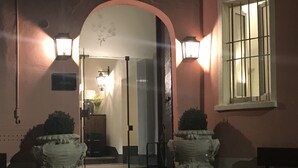 Entrada de hotel con puerta de cristal, dos macetas de piedra y un banco.
