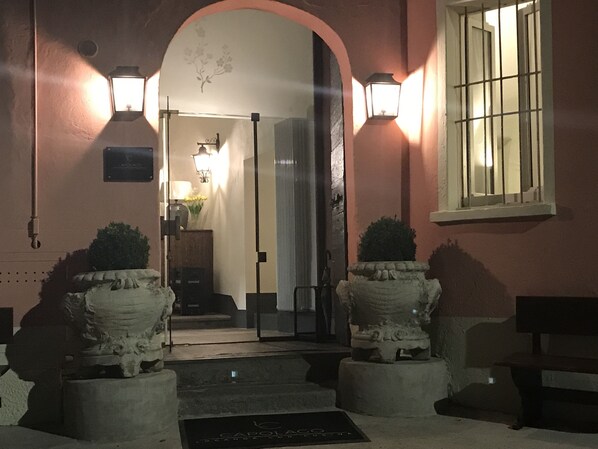 Entrada de hotel con puerta de cristal, dos macetas de piedra y un banco.
