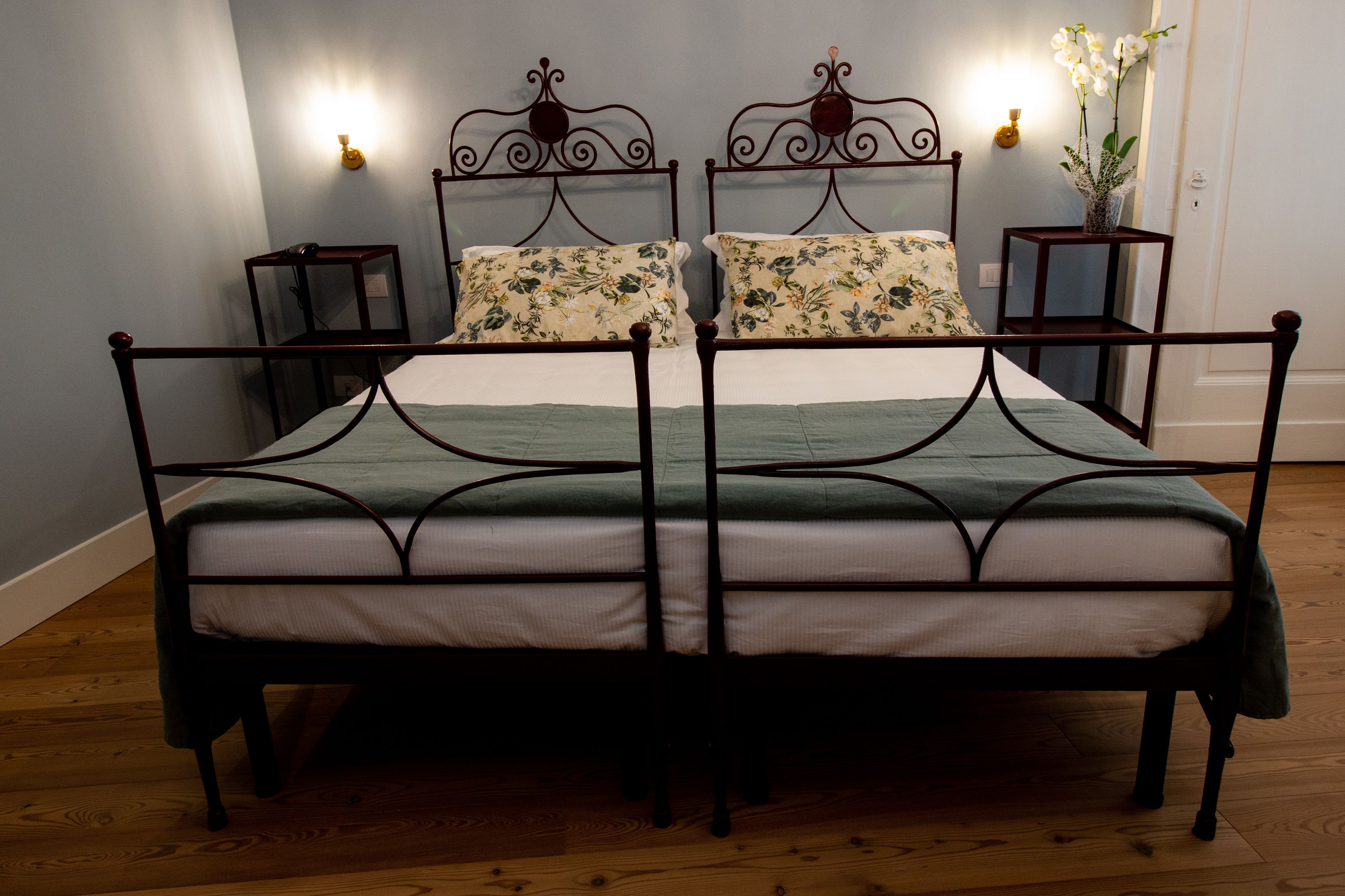 Ein Doppelbett mit einer grün-weißen Bettdecke, zwei Nachttische mit Lampen und eine Vase mit Blumen auf der rechten Seite.