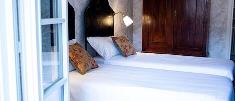 A double bed with white linens, a wooden headboard, and two floral pillows. A bedside lamp is on.