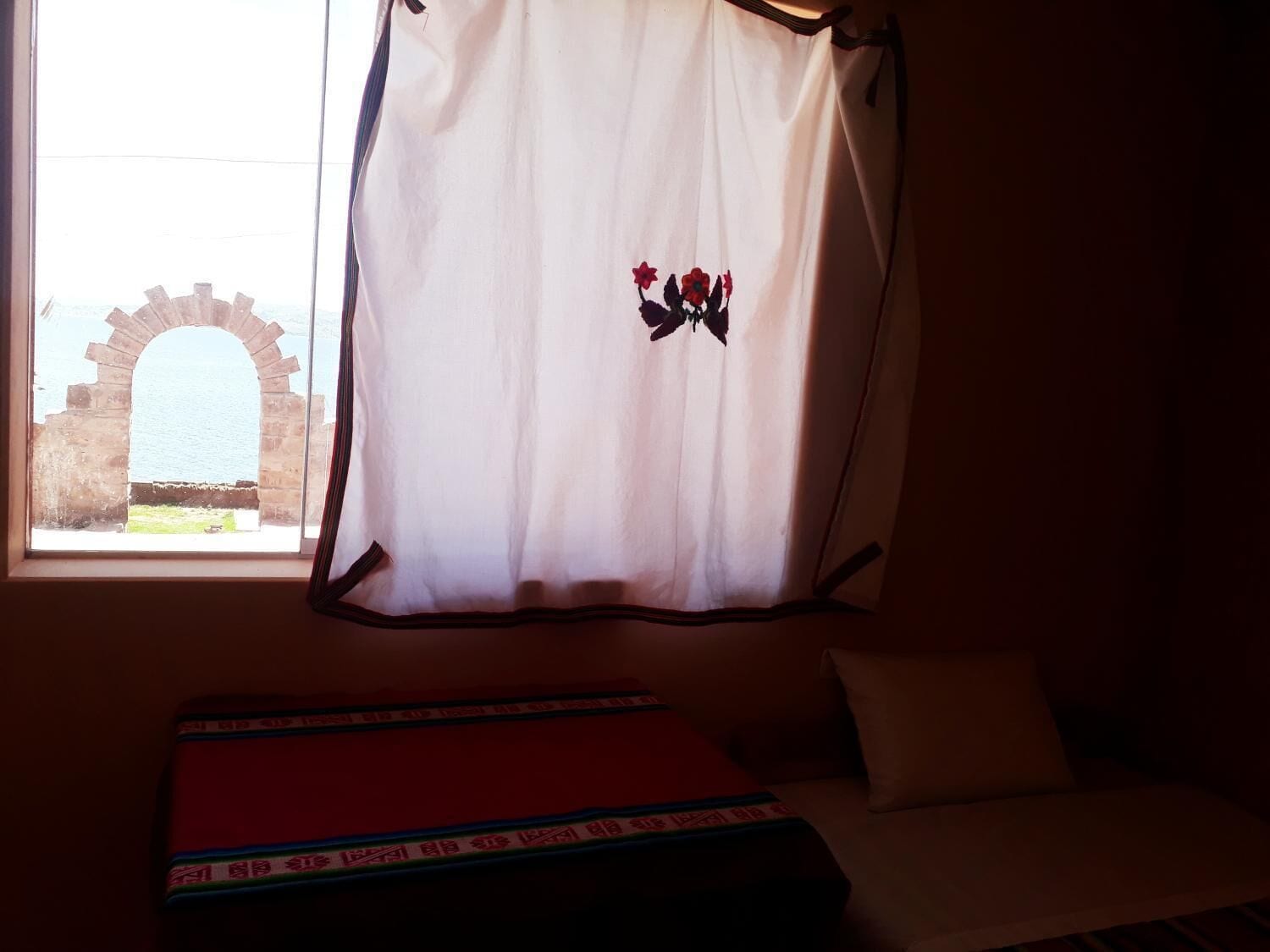 A room with a bed, a window with a curtain, and an archway view.