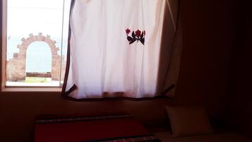 A room with a bed, a window with a curtain, and an archway view.