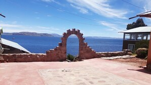 Un arc en pierre mène à une zone pavée d’où l’on peut admirer la mer et les montagnes au loin.