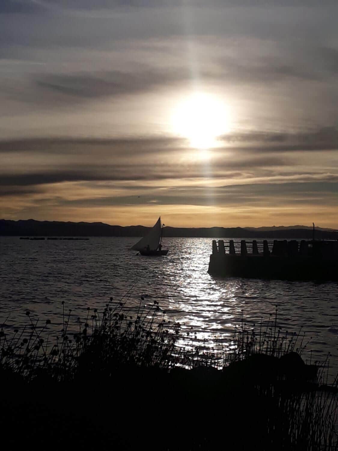 A sunset over a body of water with a sailboat and a dock.
