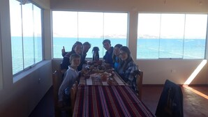Un espace repas avec une table dressée pour le repas, de grandes fenêtres offrant une vue sur la mer et un plafond haut.