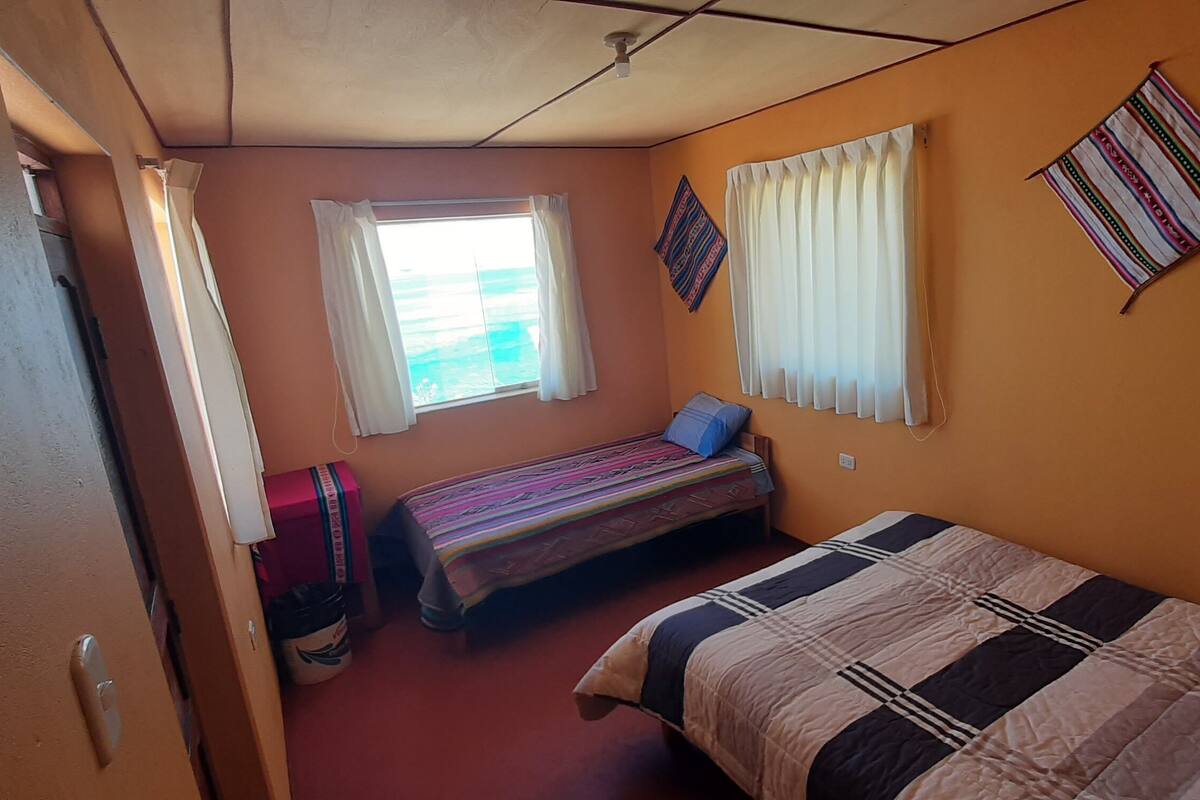 Ein kleiner, kompakter Raum mit zwei Einzelbetten, einem Fenster mit Vorhängen und einer an der Wand hängenden Flagge.