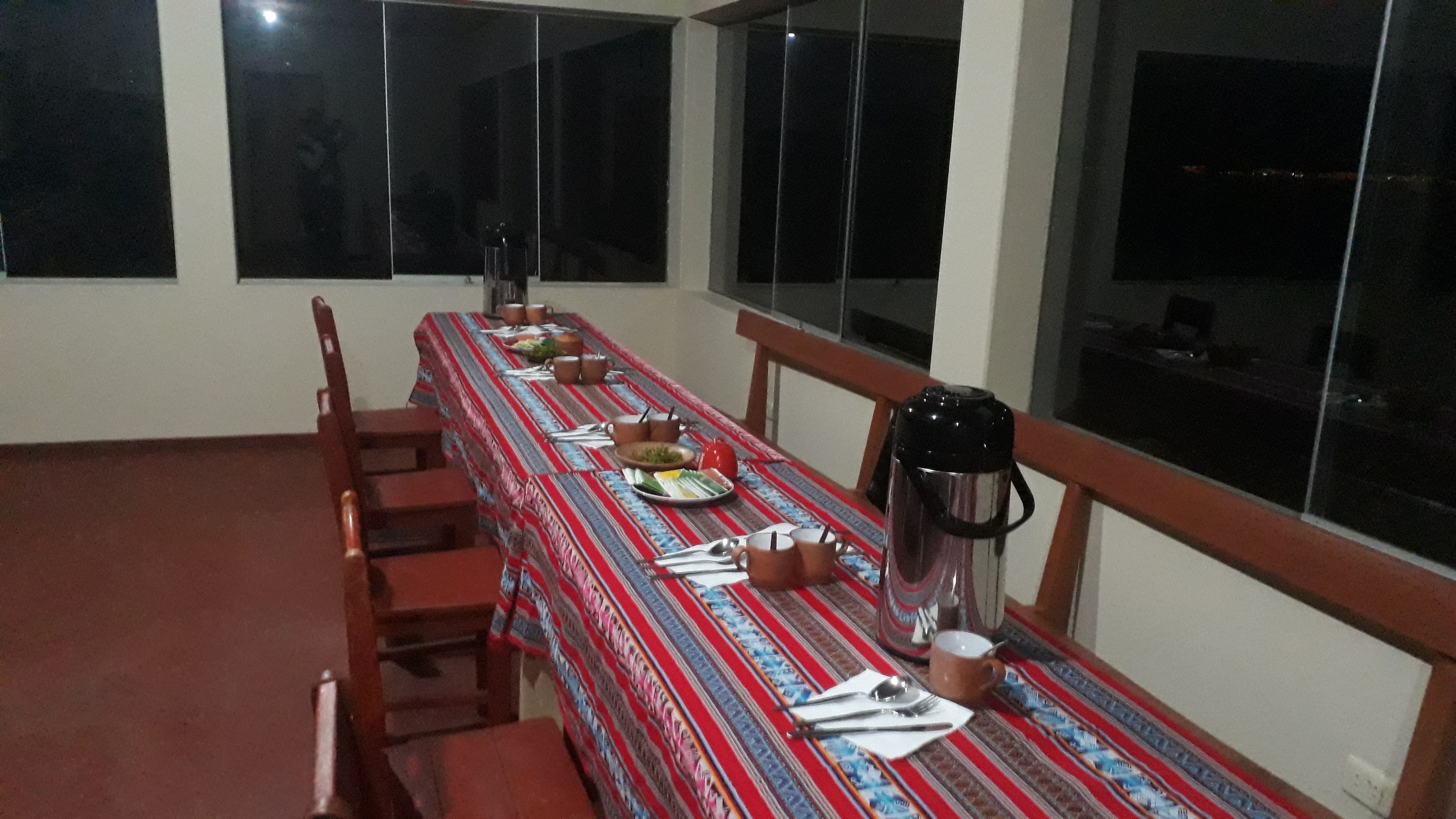Een eethoek met een lange tafel voor vier personen, compleet met borden, bekers en een thermoskan.