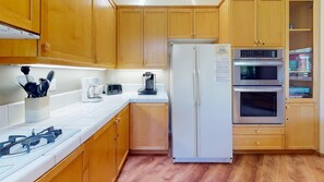 A kitchen with wooden cabinets, a white refrigerator, a coffee maker, a toaster, and an oven. - Snowcreek Resort Vacation Rental 950 (Mammoth Lakes)
